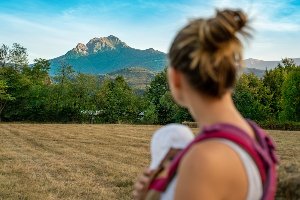 woman carrying baby facing treeline and mountain during daytime