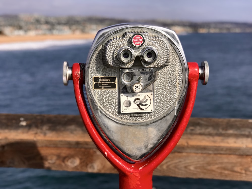 gray stainless steel and red coin-operated telescope viewing blue body of water during daytime