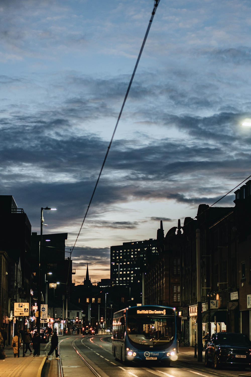 lighted blue bus near black sedan and building during dawn