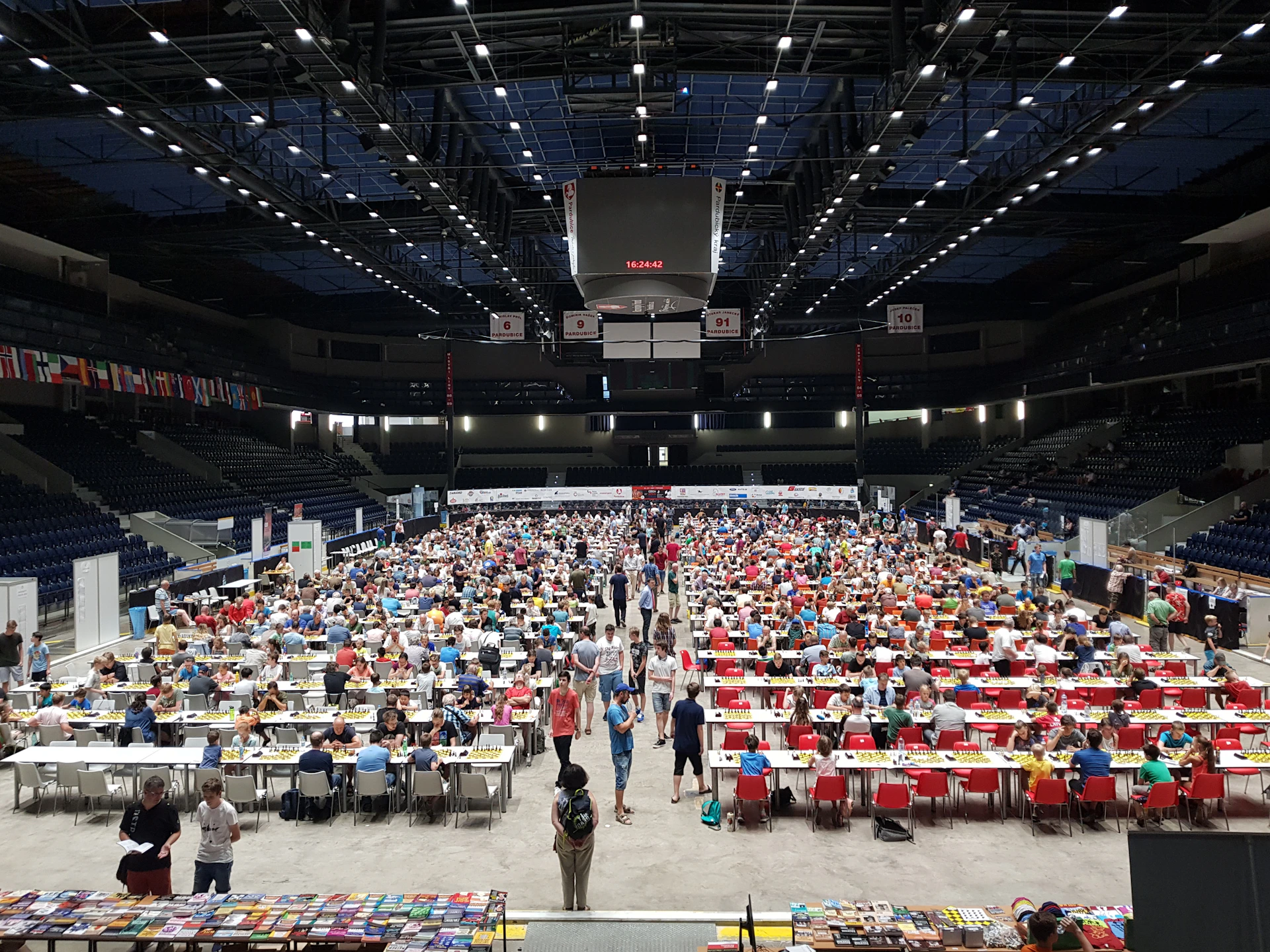 Wide shot of the crowded tournament area showing multiple beer pong tables and enthusiastic participants competing.