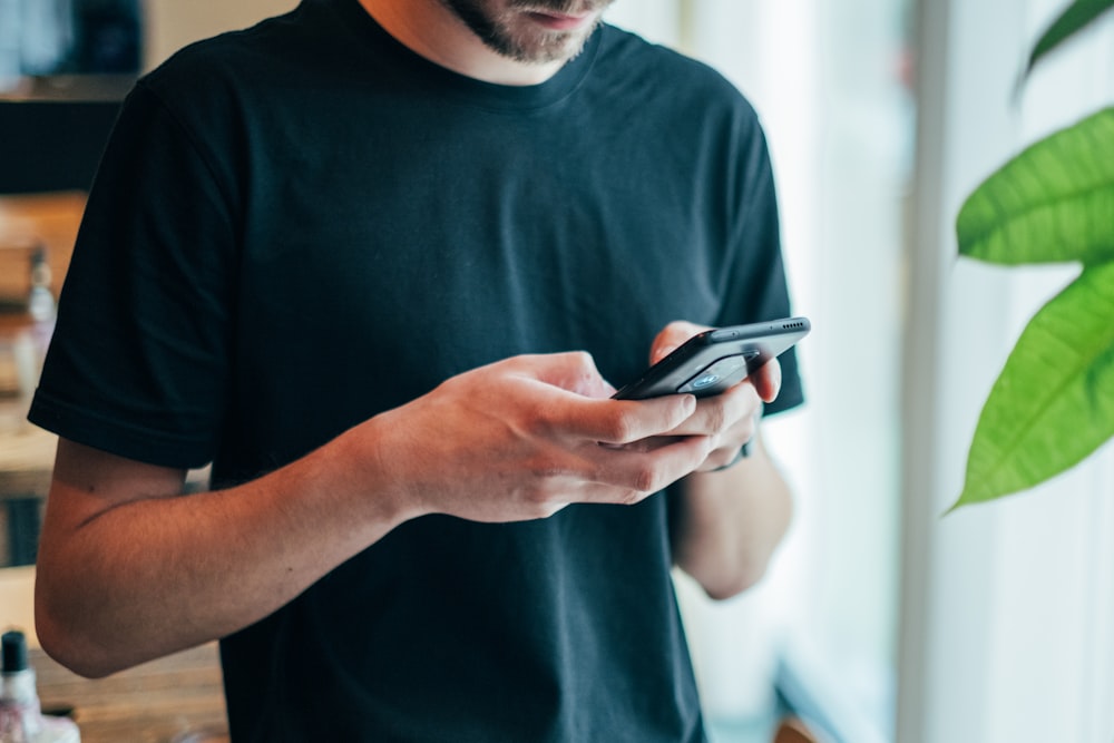 homem no top preto do pescoço da tripulação usando o smartphone