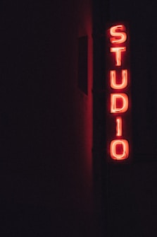 A vertical neon sign with the word 'STUDIO' glowing in bright red against a dark background.