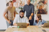 Smiling team collaborating around a laptop in a creative workspace.