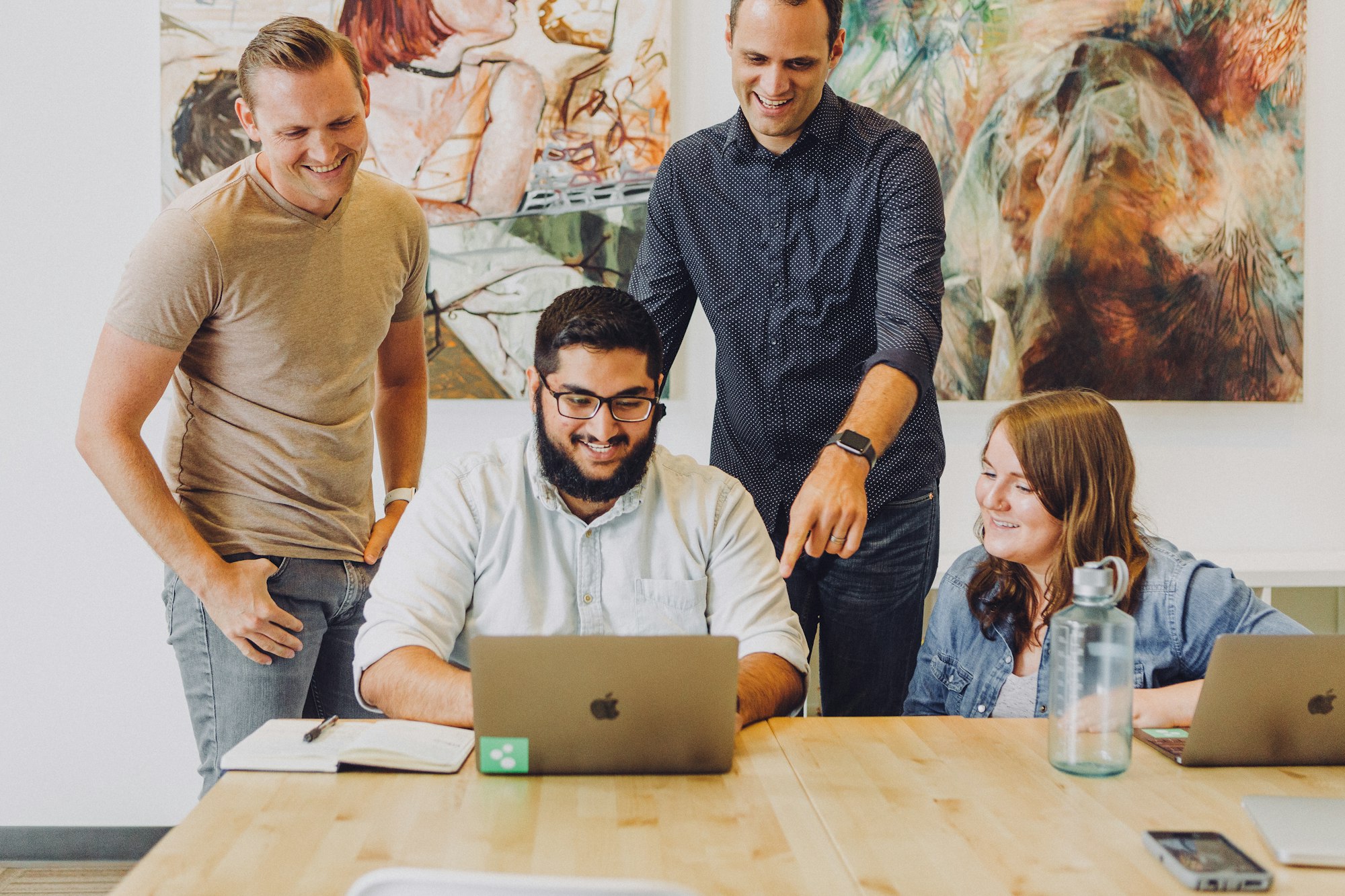 Design review in startup office with macbook and artwork. Man wearing Apple Watch. Joyful team working together and laughing.