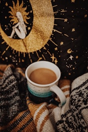 A cozy scene showing a mug with a bold, artistic print sitting beside a cushion with a matching design.