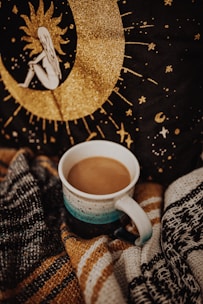 An elegant handmade ceramic mug with delicate painted details resting on a cozy knitted blanket.