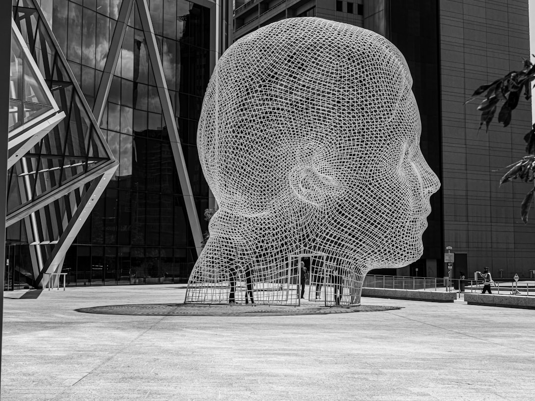 grayscale photo of mesh man bust sculpture in front of building