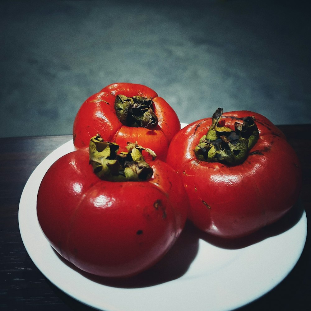 three red tomatoes on white plate