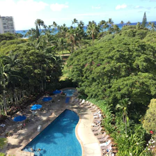 A serene swimming pool surrounded by tropical greenery with mountain and sea views.