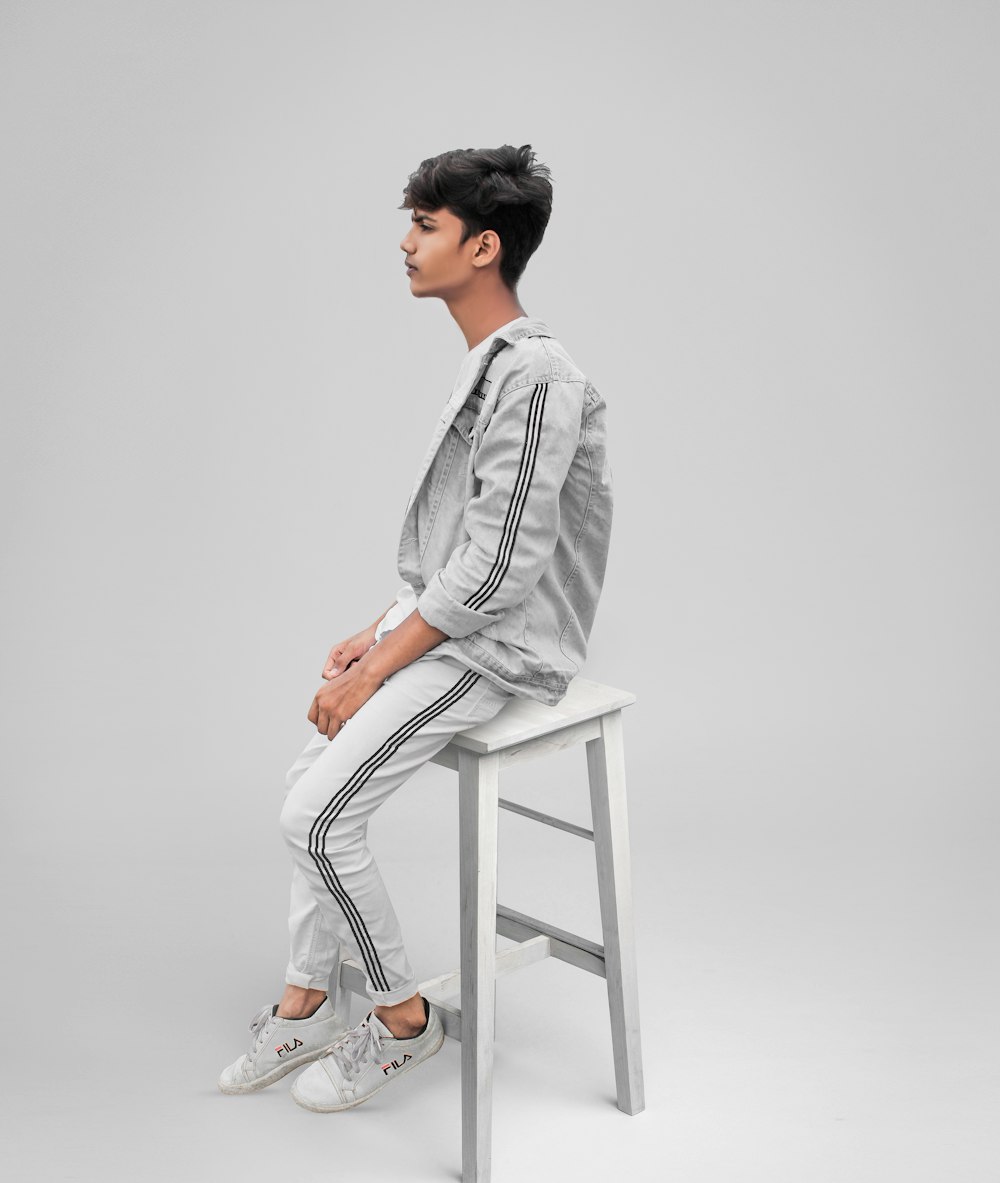 man wearing grey jacket and pants sitting on wooden stool
