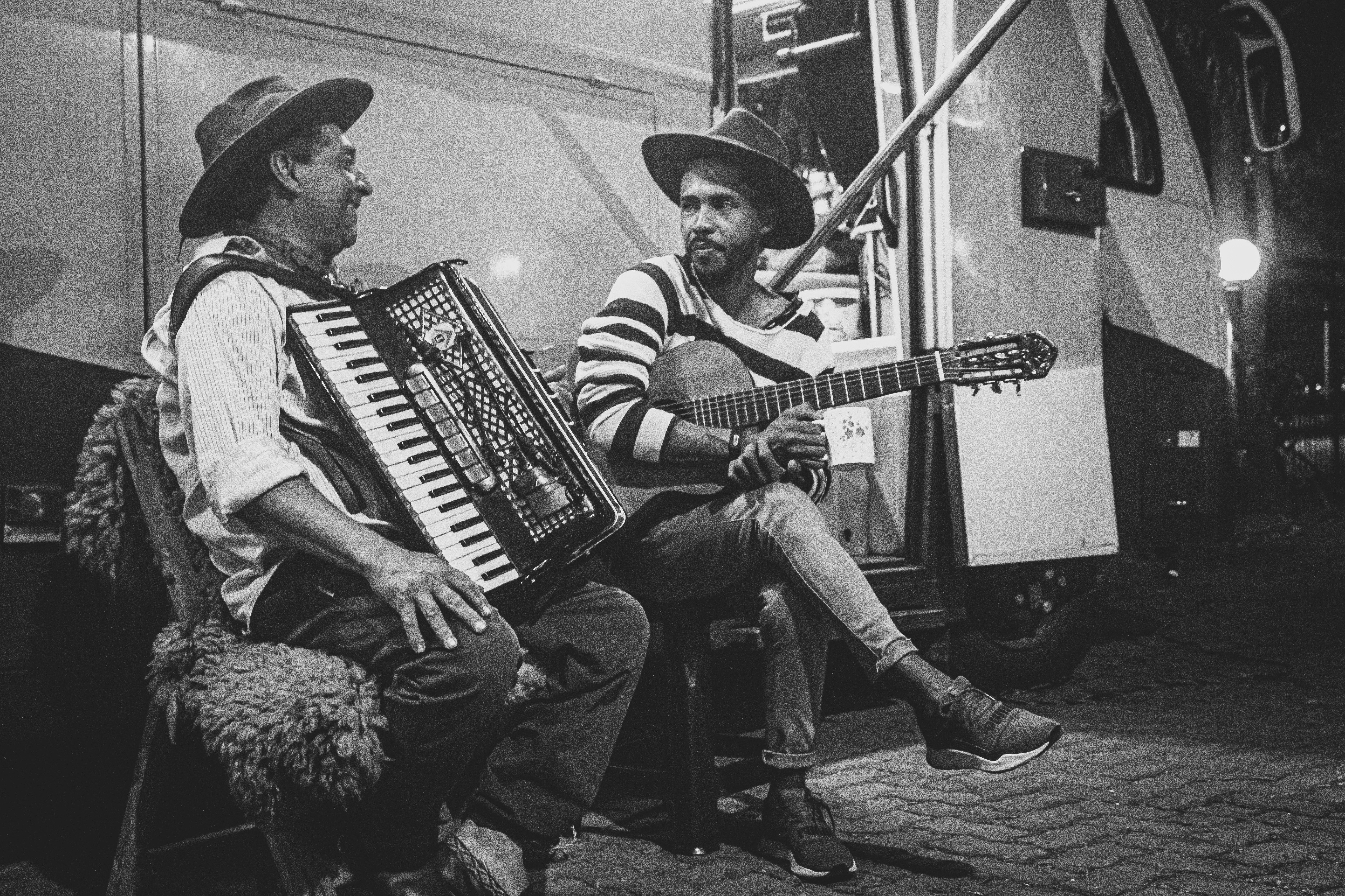 grayscale photo of two man playing musical instrument beside bus