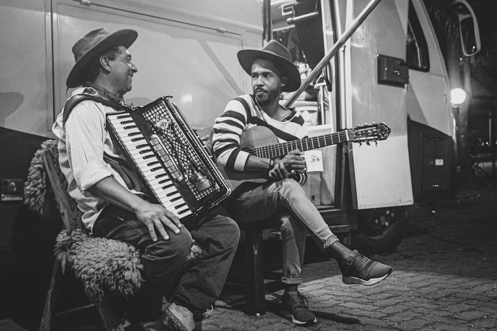 grayscale photo of two man playing musical instrument beside bus