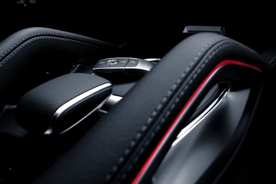 A close-up image of a car's interior focusing on the gear shift area. The design is modern and sleek, featuring a leather finish and metallic accents. A small key fob with buttons is visible, indicating functions such as lock and unlock.