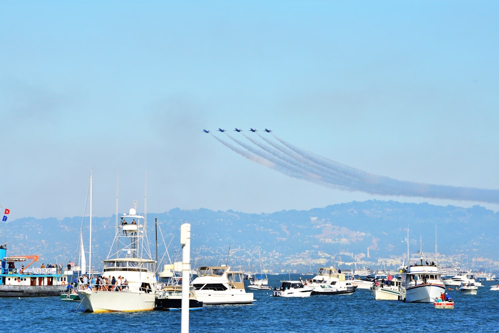 five aircraft flying over the body of water with yachts
