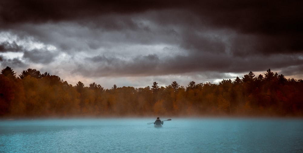 person boating on body of water under gray sky