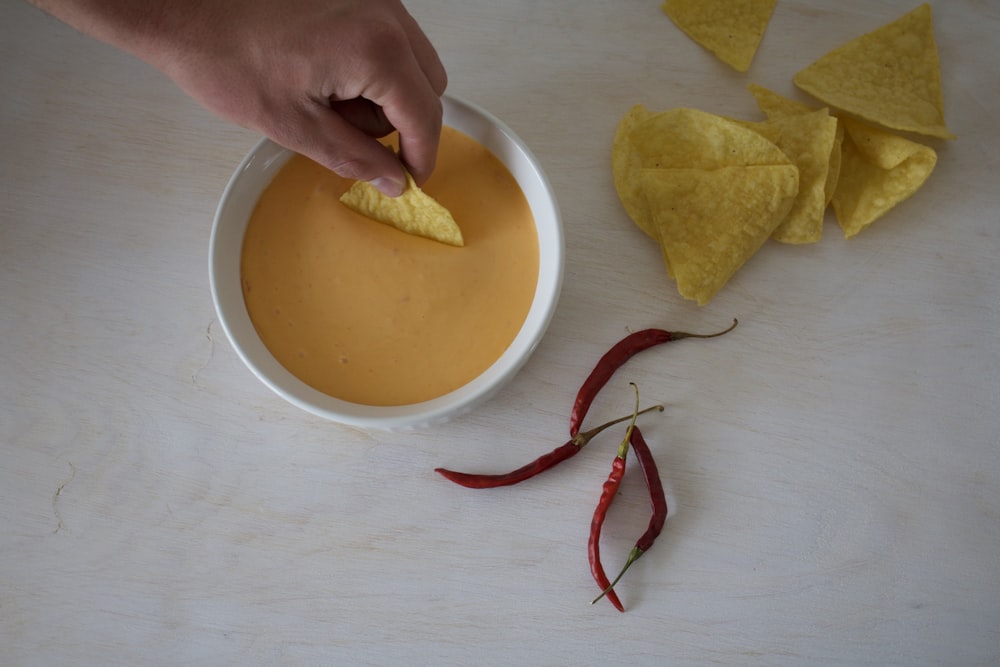 four red chills beside white cup with sauce and yellow chips