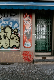 A storefront displays an illustrated panel of a woman in a polka-dot dress and top hat, titled 'Zirkus'. The adjacent wall and window feature graffiti art with abstract patterns in blue, yellow, and black. The entrance has a closed metal gate with steps leading up to it, and red graffiti is prominently visible at the bottom.