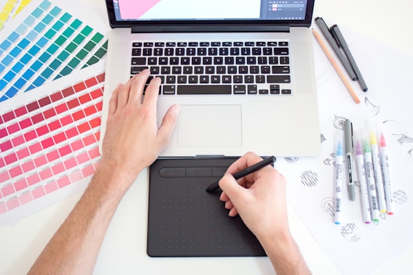 Graphic designer working on a Macbook laptop using a trackpad, color charts and markersby Theme Photos