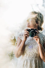 Portrait of a smiling female content creator holding a camera, set against a soft, elegant wedding backdrop.