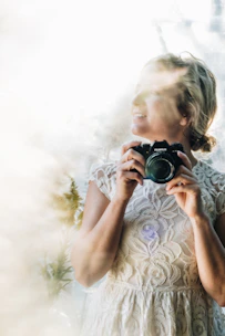 Portrait of a smiling female content creator holding a camera, set against a soft, elegant wedding backdrop.