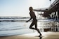 a woman is running on the beach with a surfboard