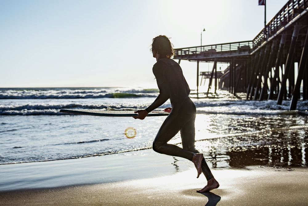 a woman is running on the beach with a surfboard