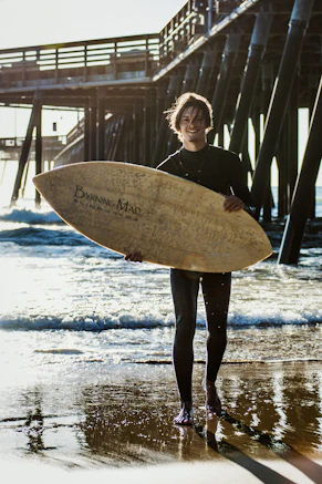 smiling man holding skimboard while standing near seashore during daytime