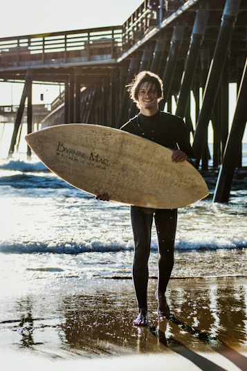 smiling man holding skimboard while standing near seashore during daytime