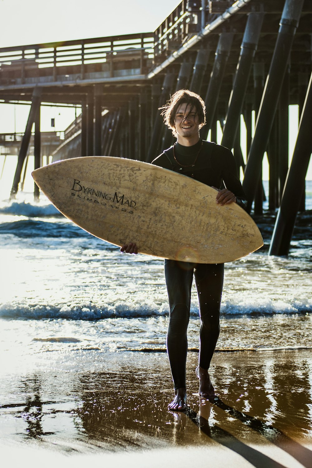 Uomo sorridente che tiene la tavola da surf mentre si trova vicino alla riva del mare durante il giorno