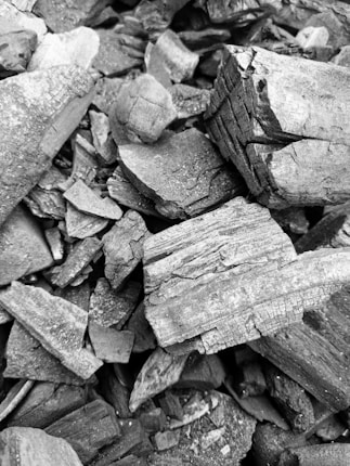 A collection of rough, jagged charcoal pieces of various sizes and shapes, creating a textured and irregular surface.