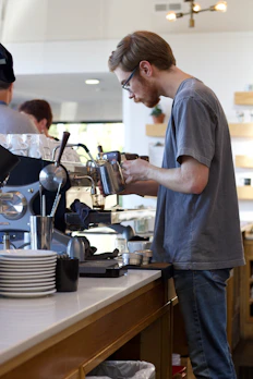 Barista steaming milk with vixn coffee shop sign in the background.