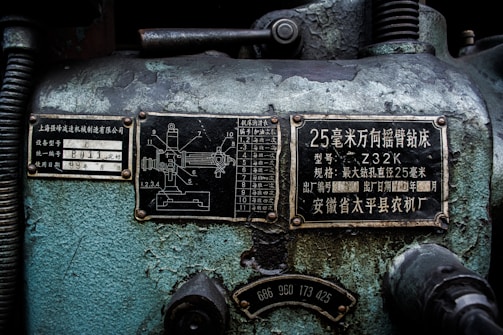 A close-up view of an industrial machine panel with various Chinese characters and numerical labels. The surface displays wear and crackling paint, suggesting age and use. There are two metal plates with technical diagrams and descriptions, along with numbers and letters in white on a black background.
