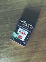 A package of Ricola Forest Blossom Swiss Herb Lozenges is placed on a wooden surface. The packaging features floral imagery and text indicating it is sugar-free.