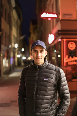 Model wearing a black streetwear jacket under city neon lights at night.