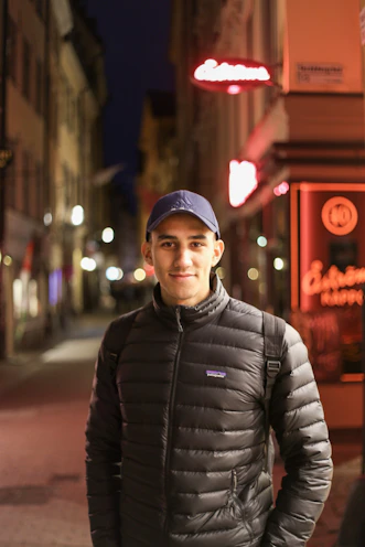 Model wearing a black streetwear jacket under city neon lights at night.