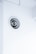 A circular ventilation duct is embedded in a white wall, featuring a series of concentric rings inside the vent. The surrounding area is clean and minimalistic with an overall bright appearance.