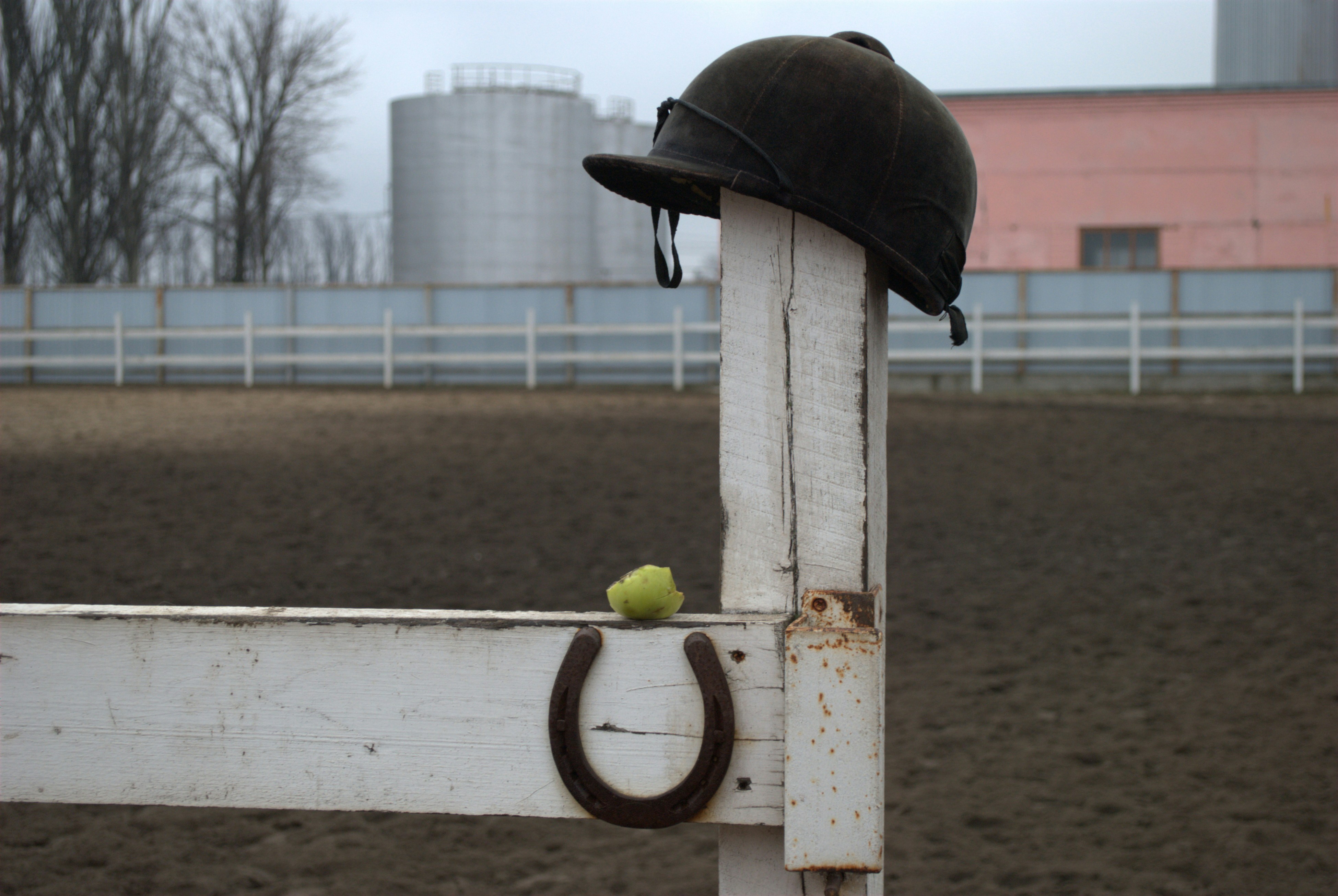 A sleek equestrian helmet resting on a wooden fence in a sunny stable.