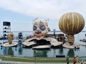 A colorful stage setup with a clown performing juggling acts, featuring red and blue accents and a white backdrop