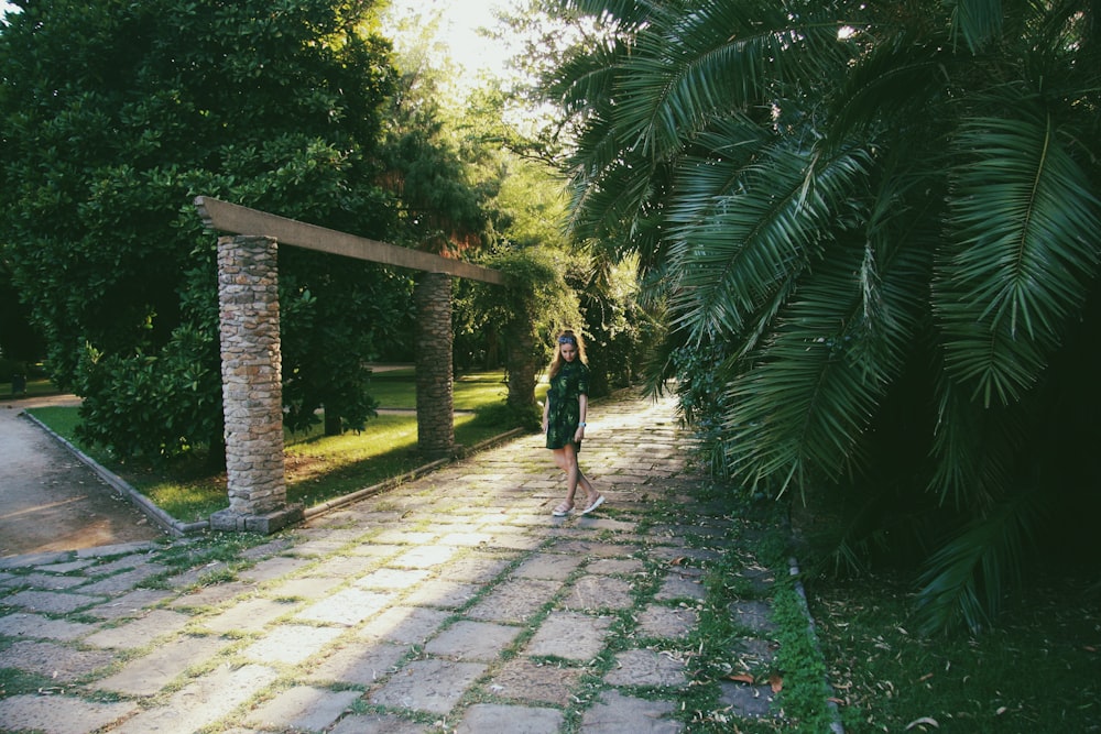 woman standing on pathway surrounded with tall and green trees during daytime