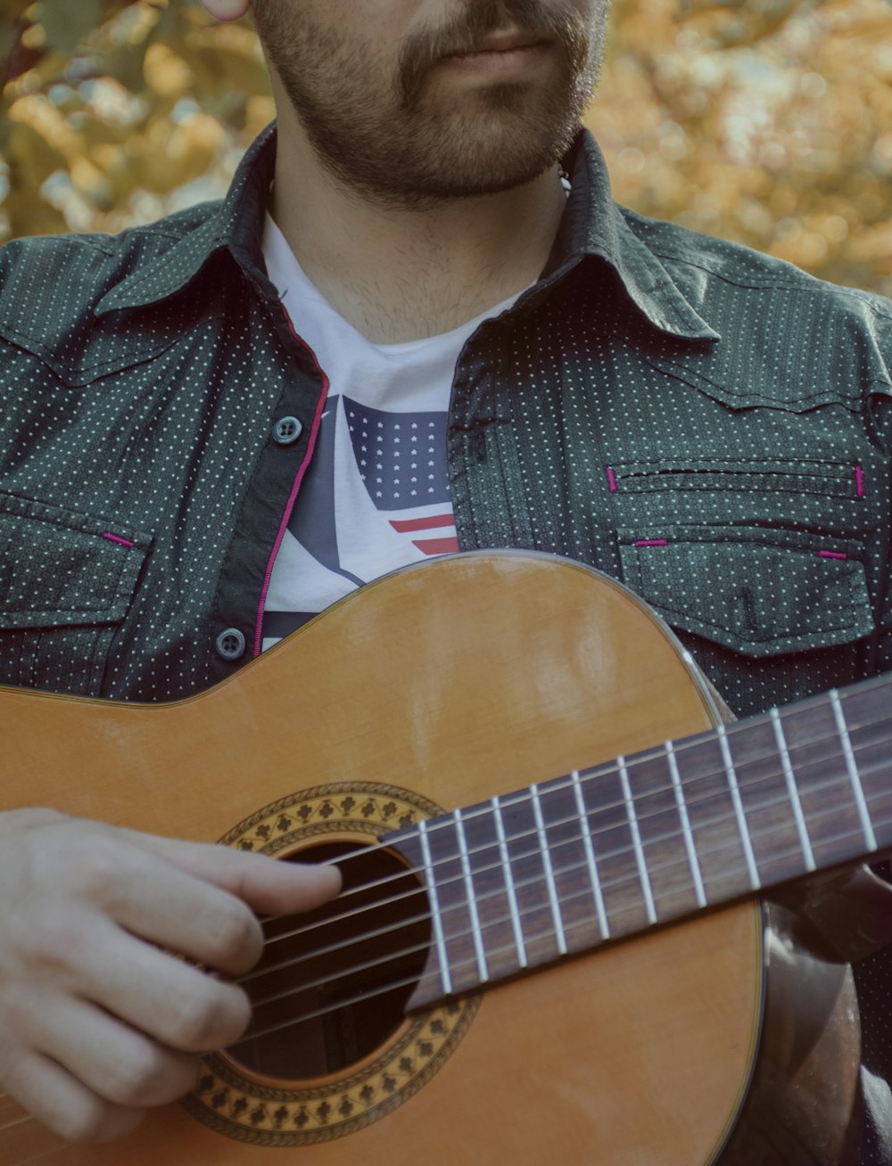 man wearing green and white polka-dot collared button-up shirt playing brown guitar