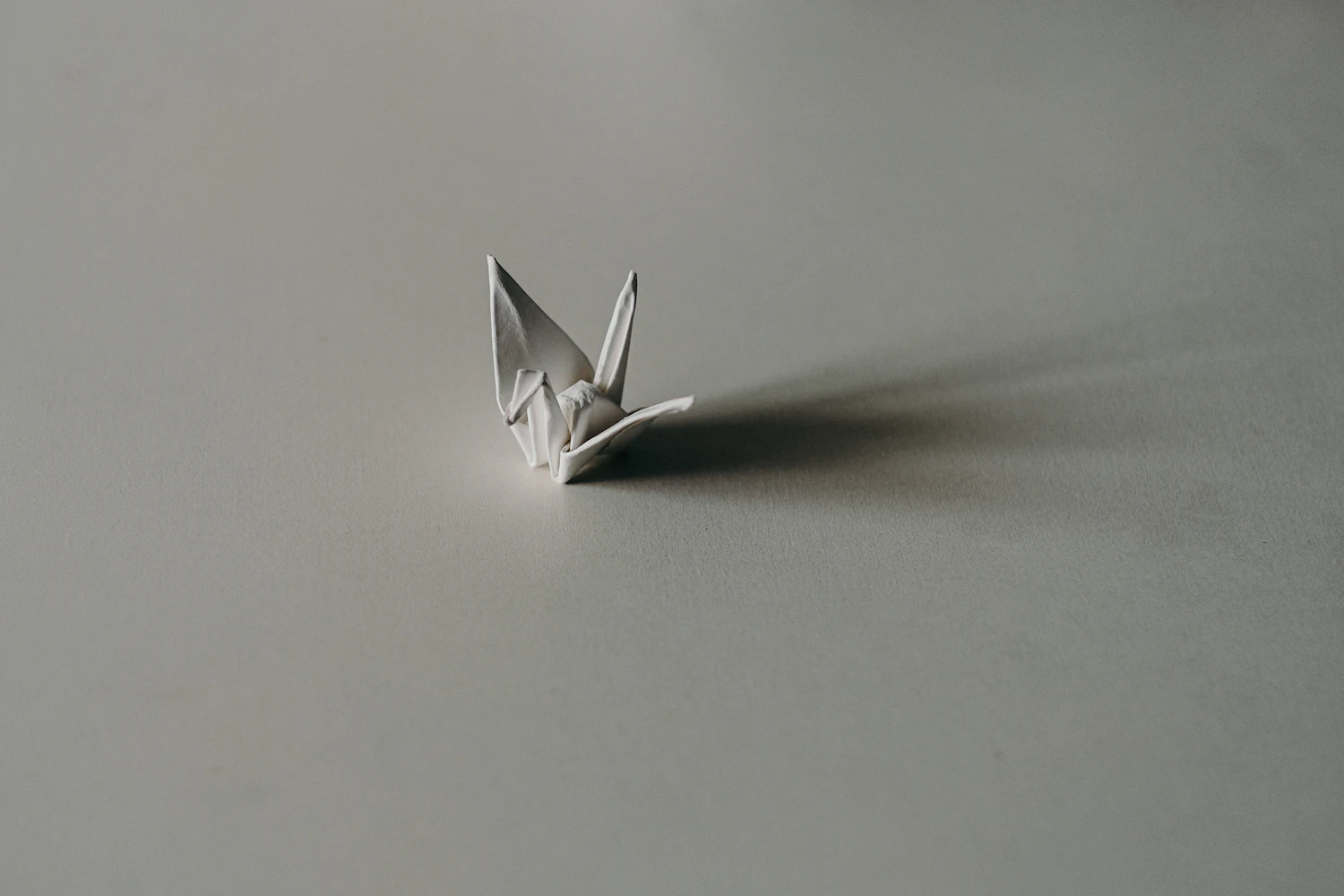 A finished white paper crane standing on a pale grey surface