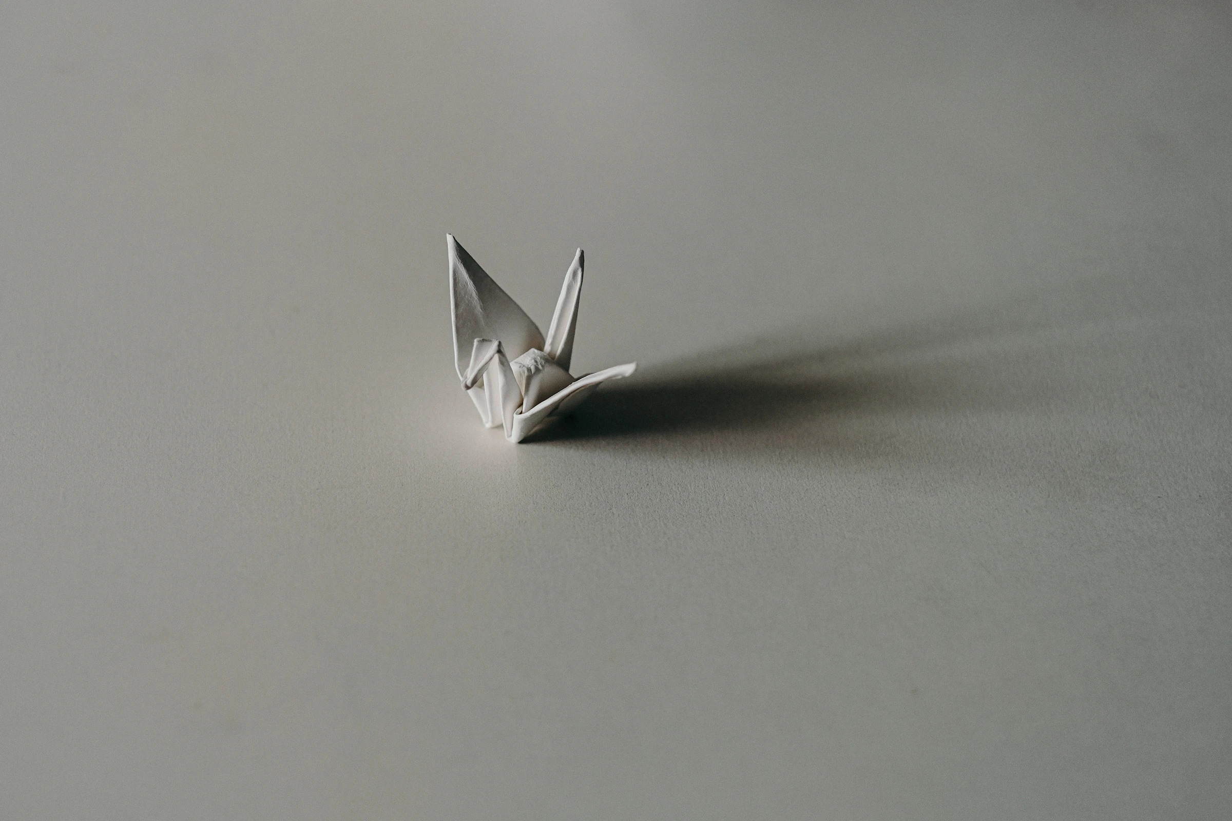 A grey paper origami crane sitting on a flat panel, evoking precise, repeatable construction.