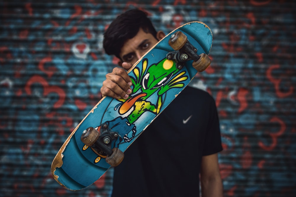 shallow focus photo of man holding blue skateboard