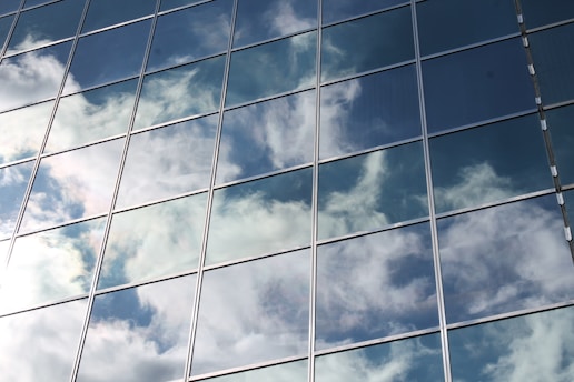 Reflections of clouds and the blue sky are visible on the surface of a glass building with multiple window panes.