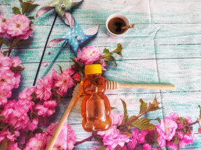 Photograph of a rustic wooden table with natural honey jars and fresh mountain flowers beside a handwritten note.