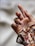 A hand with neatly manicured nails painted in a rich, glossy red color. The nails have intricate patterns, and the wrist is covered by a floral, patterned fabric in earthy tones.