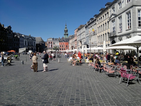 A panoramic view of a historic city square bustling with locals and tourists under clear blue skies.