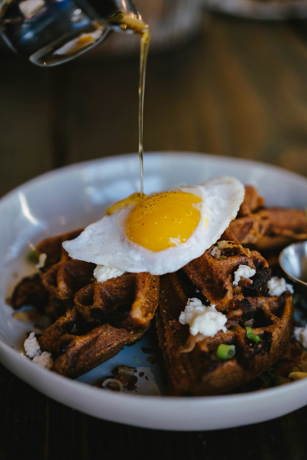 person pouring maple syrup on bowl of waffle with sunny side up egg