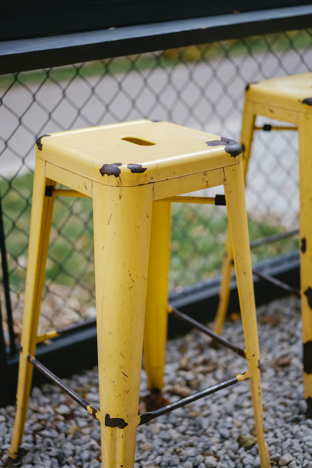two empty yellow stools beside mesh fence