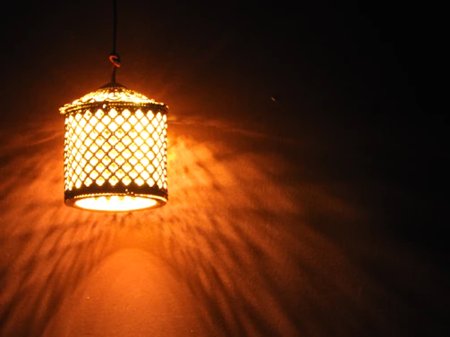 An elegant brass lantern casting intricate shadows on a whitewashed wall.